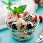 glass jar of fresh berries with custard sauce, whipped cream and mint