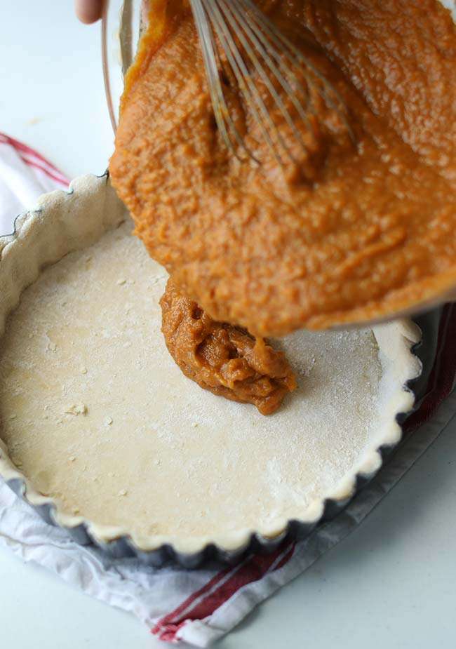 pouring a sweet potato pie filling into a pie crust