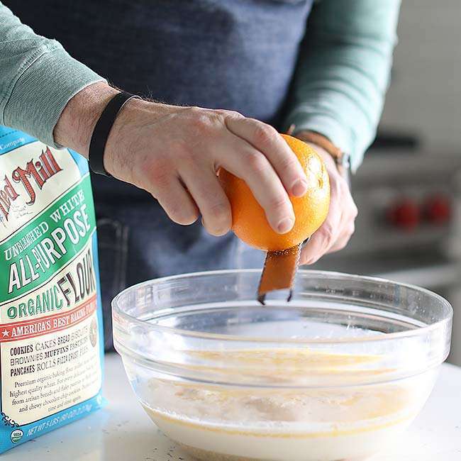 adding orange zest to a bowl with yeast and milk