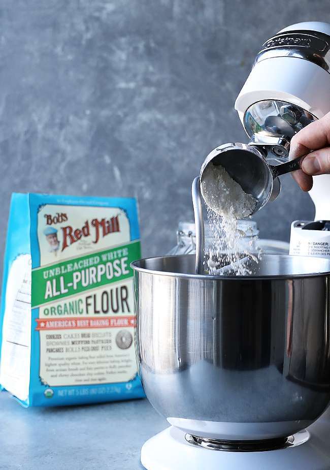 adding flour to a stand mixer with the hook attachment