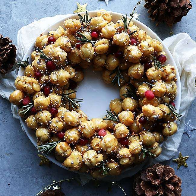 Homemade Struffoli Recipe with Honey and Pecans on a plate and decorated with rosemary, sprinkles and cranberry