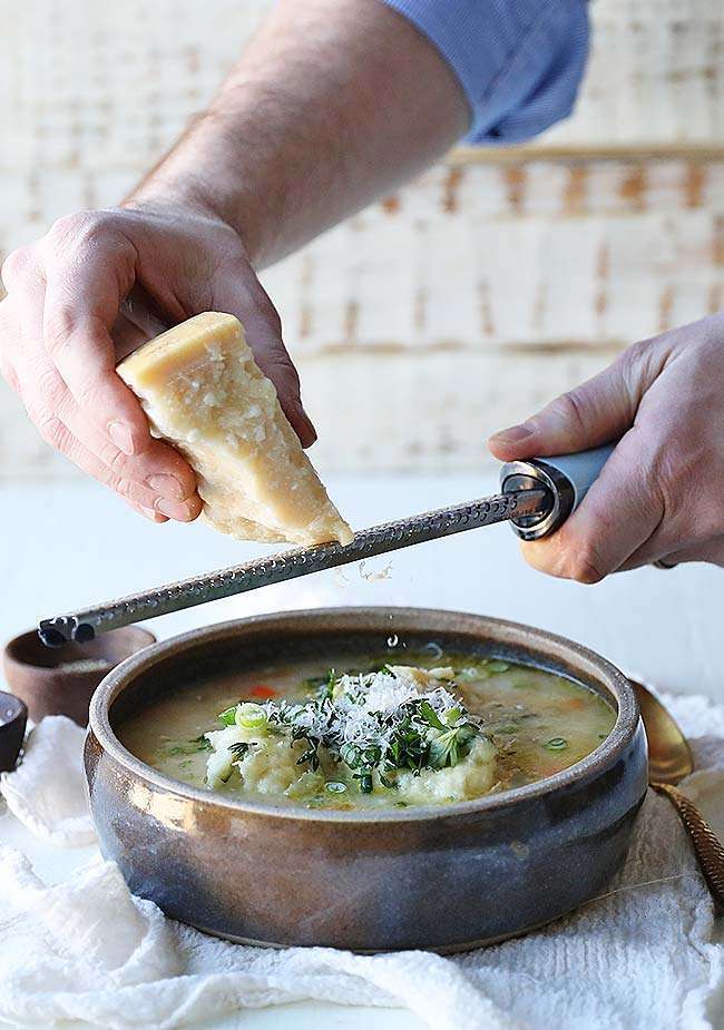 shredding fresh parmesan cheese into a bowl of chicken dumpling soup