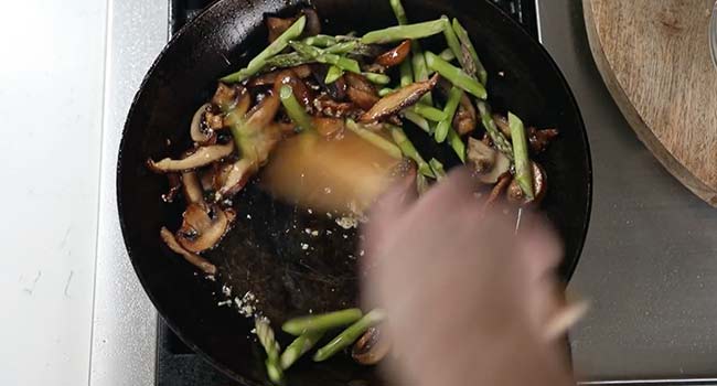stirring asparagus into a pan with mushrooms