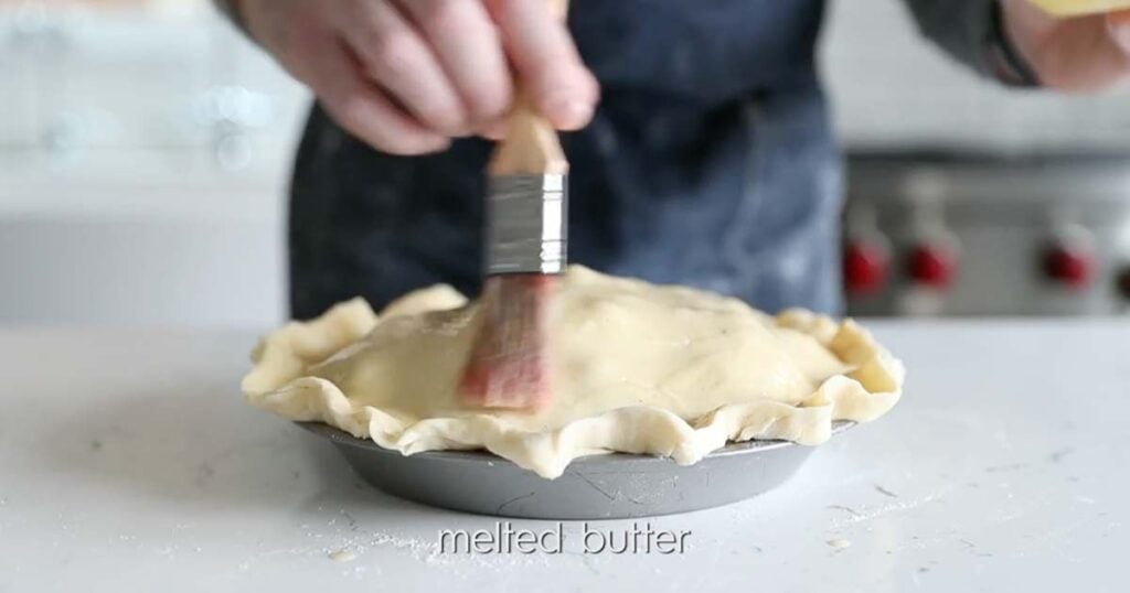 brushing a blueberry pie with melted butter