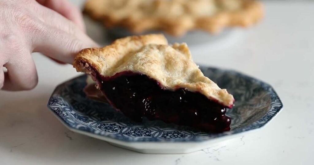 adding a slice of blueberry pie to a plate