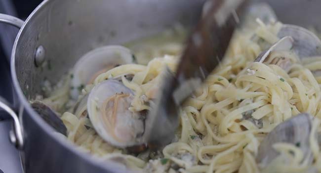 mixing together cooked clams and cooked pasta