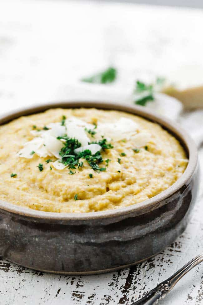 bowl of creamy polenta that is topped of with shredded parmesan and parsley