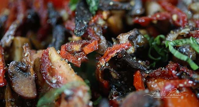 adding basil and tomatoes to mushrooms