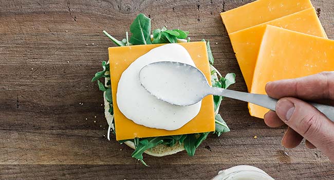 adding cheese and creamy horseradish sauce to a bun