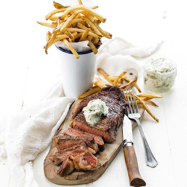 sliced steak with butter and fries on a cutting board