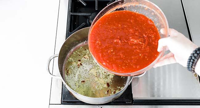 adding crushed tomatoes to a pot of garlic and chiles