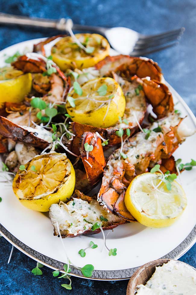 grilled lobster tails on a platter with lemons