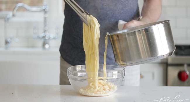 adding cooked fettuccine to a bowl of butter and cheese