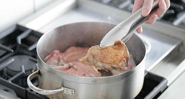 searing a whole chicken in a large pot to golden brown