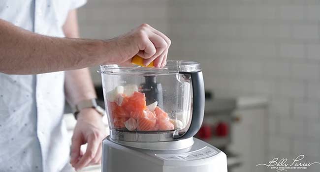 adding lemon to a food processor with salmon