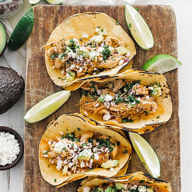 cutting board with 3 chicken tinga tacos and limes