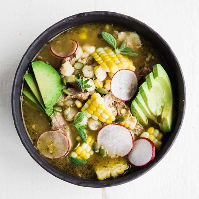 verde pork posole recipe in a bowl served with corn and avocado