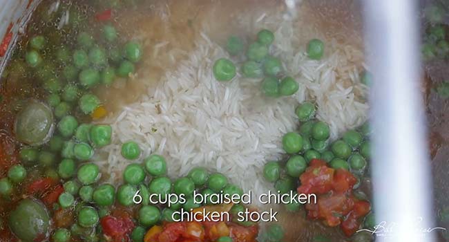 adding chicken stock to a pot with rice