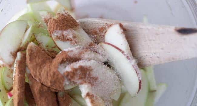 mixing sliced apples with cinnamon and sugar in a bowl