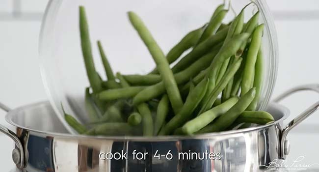 adding green beans to a pot of boiling salted water