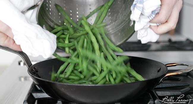 adding cooked green beans to a pan