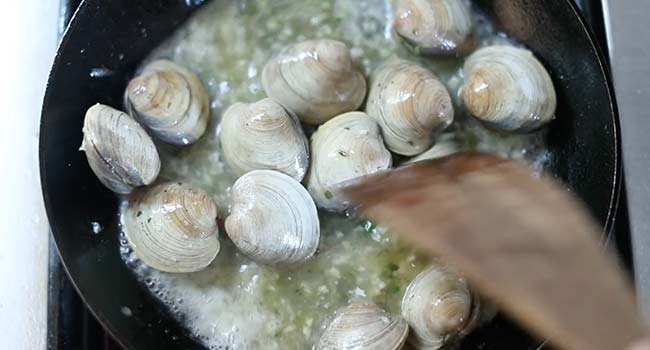 adding wine to clams in a pan