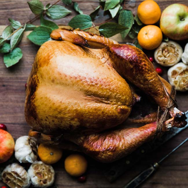 smoked and brined turkey recipe on a cutting board with fruit and roasted garlic