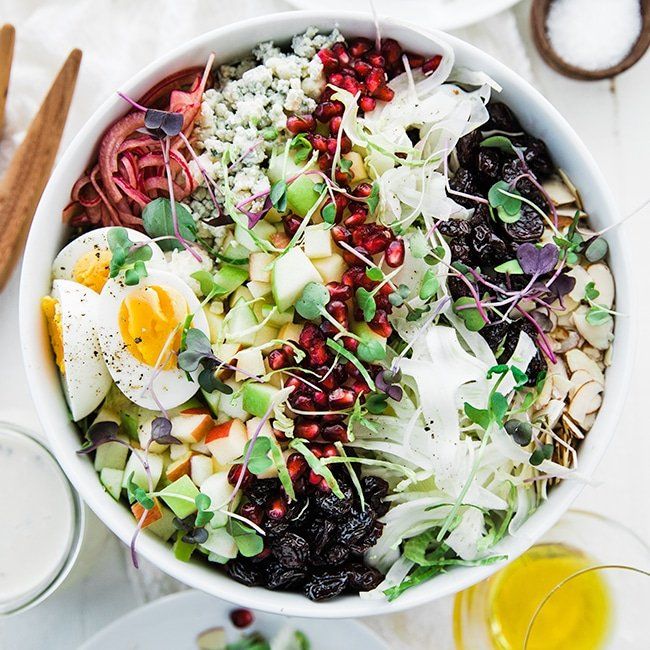 shaved brussel sprout salad in a bowl with hard boiled eggs, apples, pickled onions, blue cheese and fennel