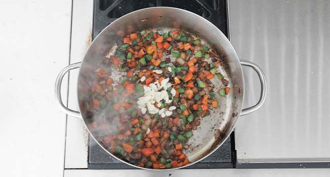 adding garlic to peppers and onions