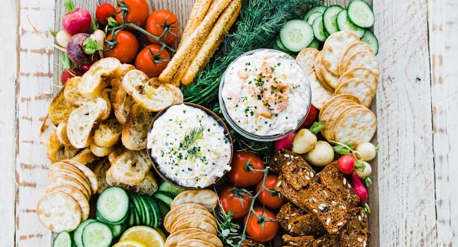 smoked salmon dip on a cutting board with crackers and vegetables