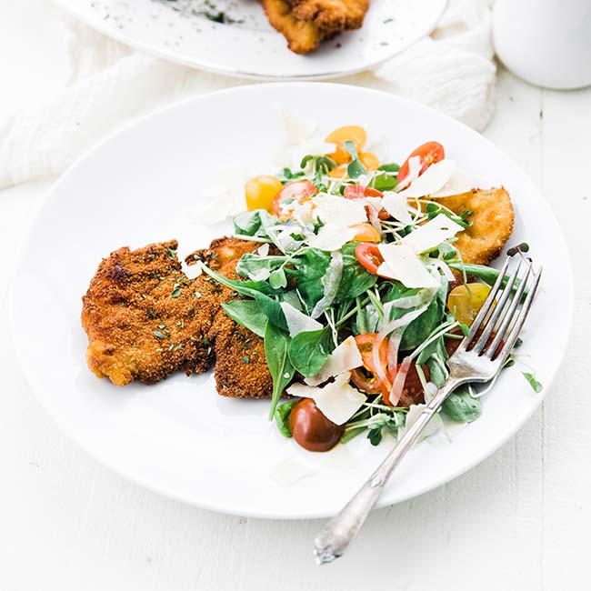 chicken milanese recipe with an arugula salad and parmesan cheese on a plate