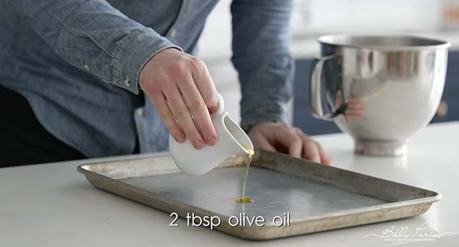 pouring olive oil onto a sheet tray