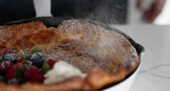 sprinkling powdered sugar onto a dutch baby