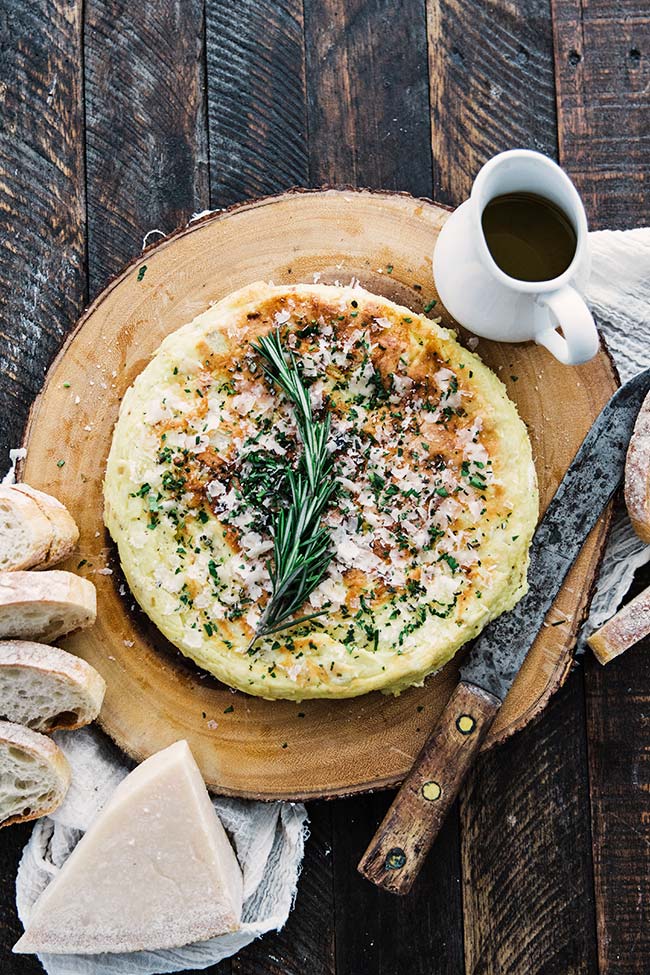 whole frittata on a cutting board with rosemary and cheese