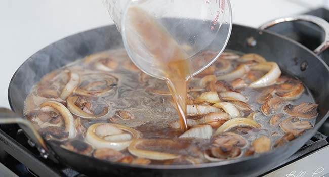 adding beef stock to mushrooms and onions