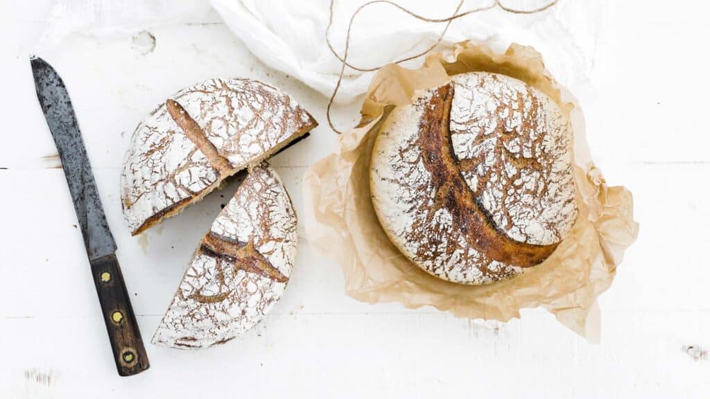 sliced spelt bread and whole bread loaf with knife and parchment paper