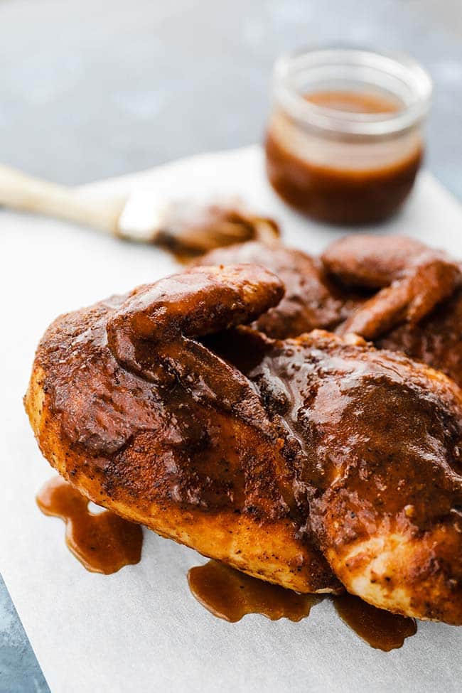 smoked chicken halves covered in bbq sauce with sauce on the side