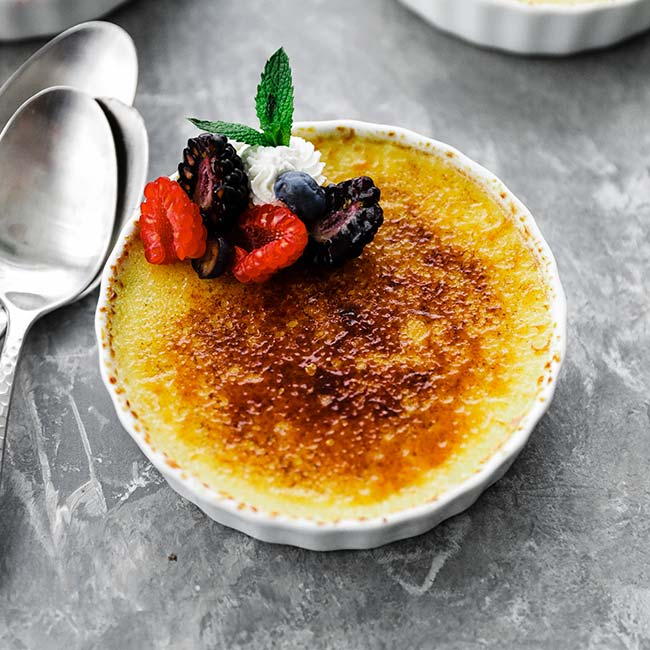 creme brulee in a white dish with fresh berries, whipped cream and mint