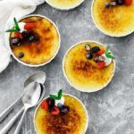 5 creme brulees with spoons served with berries and whipped cream