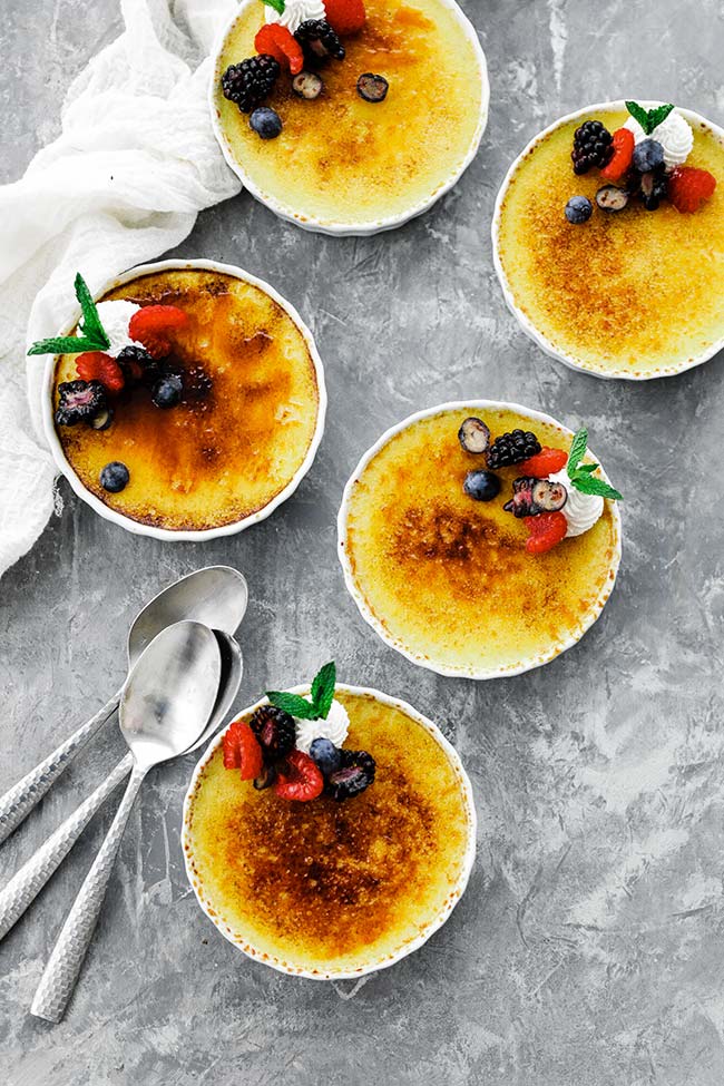 5 creme brulees with spoons served with berries and whipped cream
