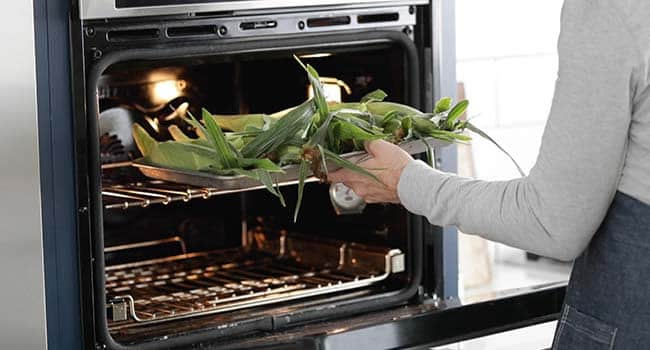 adding corn un husked on a tray to an oven