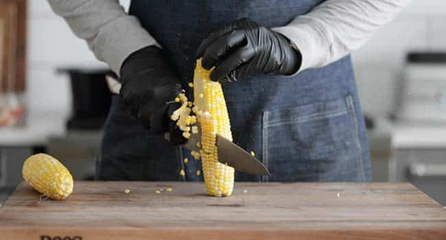 slicing cooked corn off of the cob