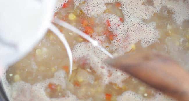 adding a slurry to a pot of corn chowder