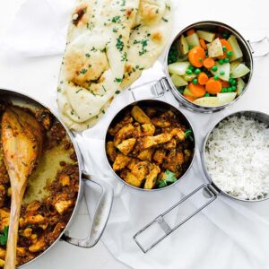 curry chicken in tiffin boxed with rice, naan and vegetables