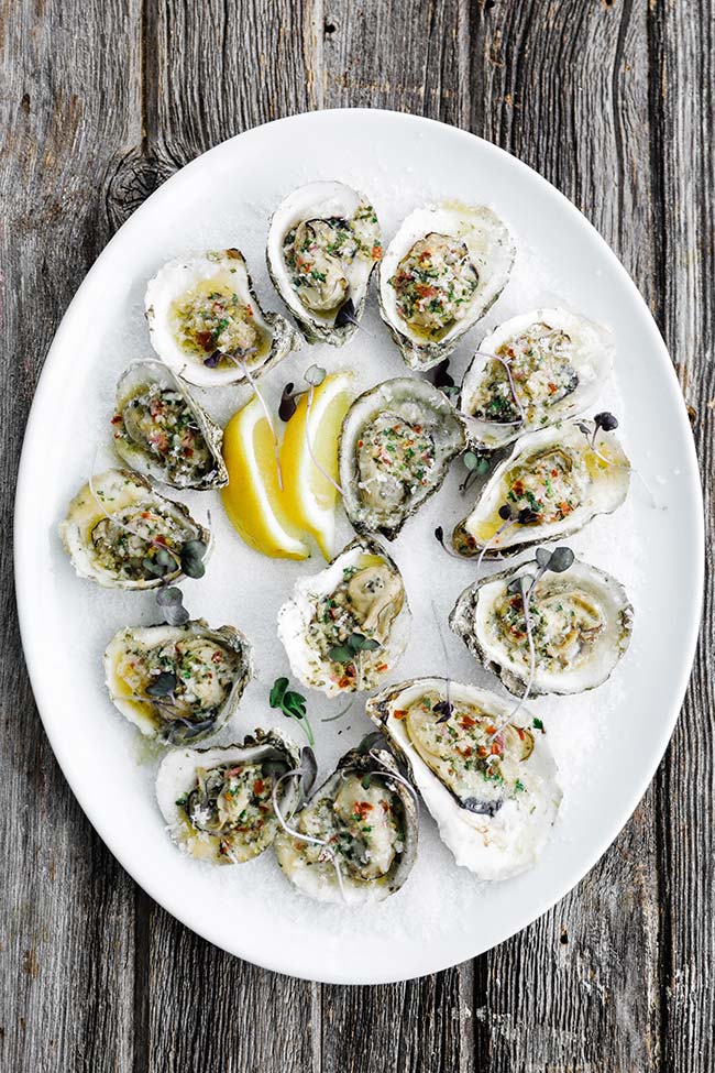 plate of grilled oysters over salt with lemons and butter