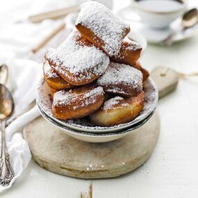 bowl of donut beignets that has been dusted with powdered sugar