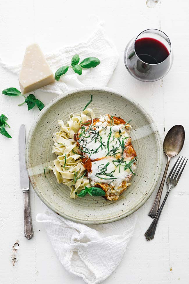 chicken parmesan on a plate with noodles, cheese and wine