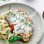 cheese and tomato on chicken with noodles on a plate with red wine