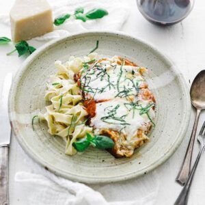 chicken parmesan with basil on a plate with buttered noodles