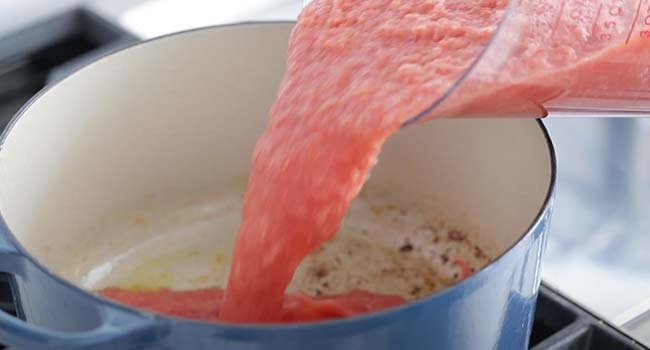 pouring pureed tomatoes into a pot